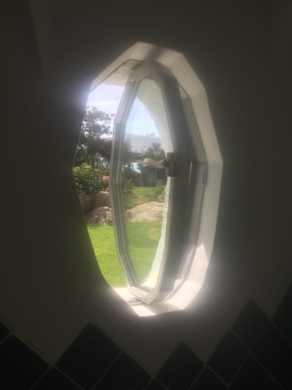 Finestra ottagonale inondata di luce solare, che mostra un giardino verde all'esterno e le piastrelle scure degli interni sottostanti.