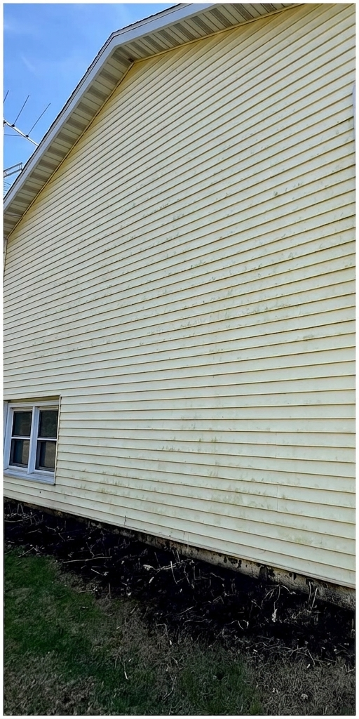 Side of a pale yellow vinyl-sided house with a window and gravel ground below
