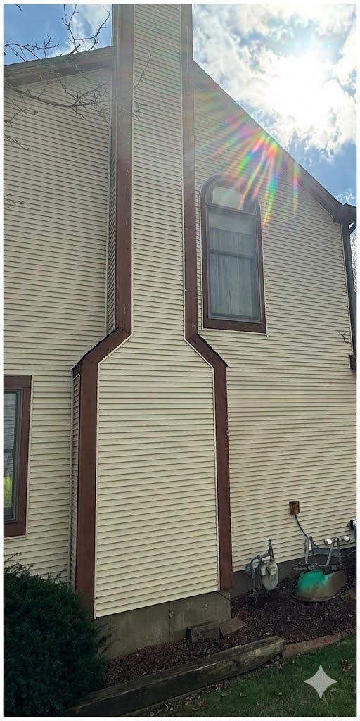 Side view of a beige house with brown trim, a narrow window, and bright sun flare in a blue sky.