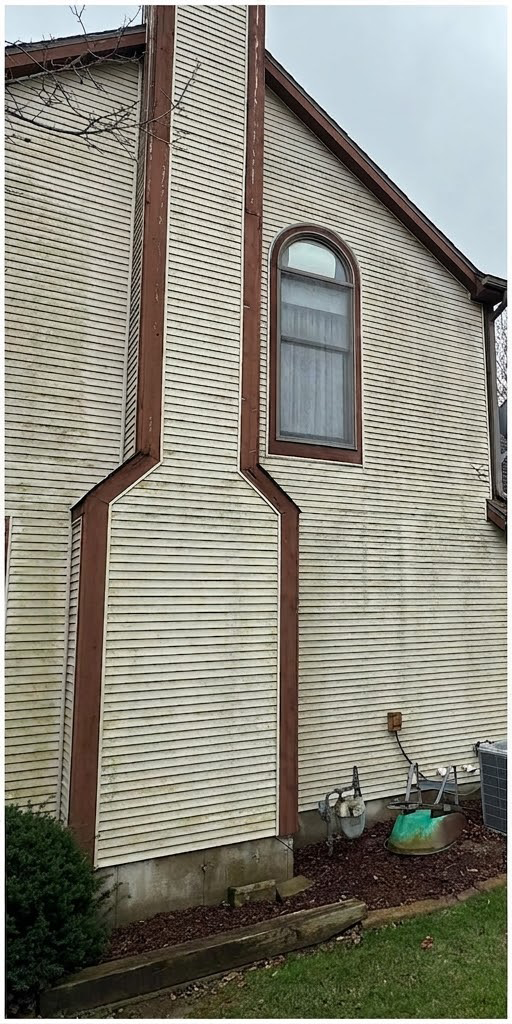 Side of a beige house with brown trim, lattice vent, arched window, and a sloped roof near a grassy yard.