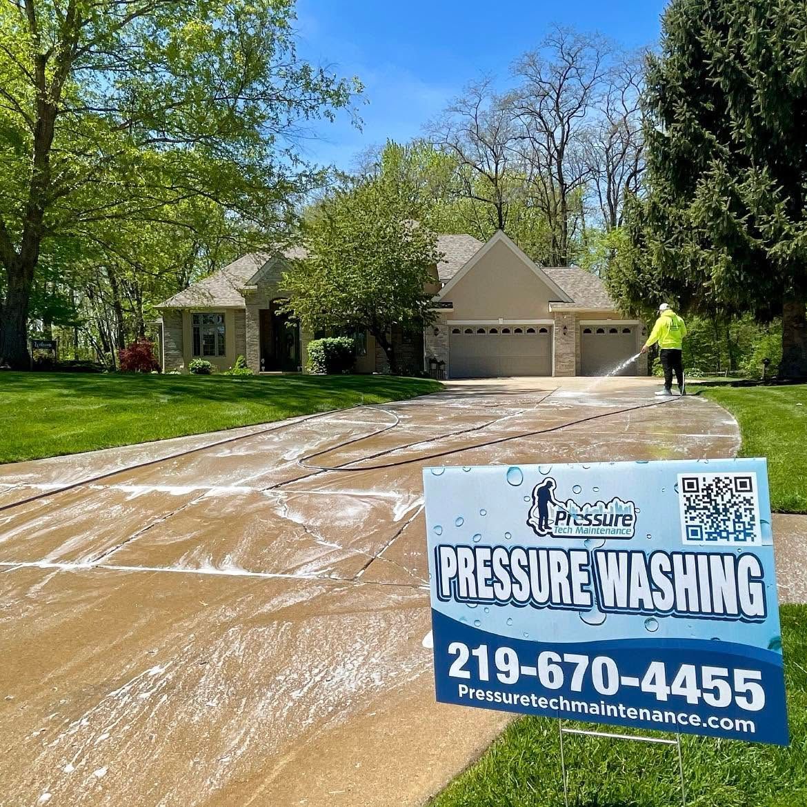 Pressure washing driveway in front of a suburban house; business sign with phone number in foreground.