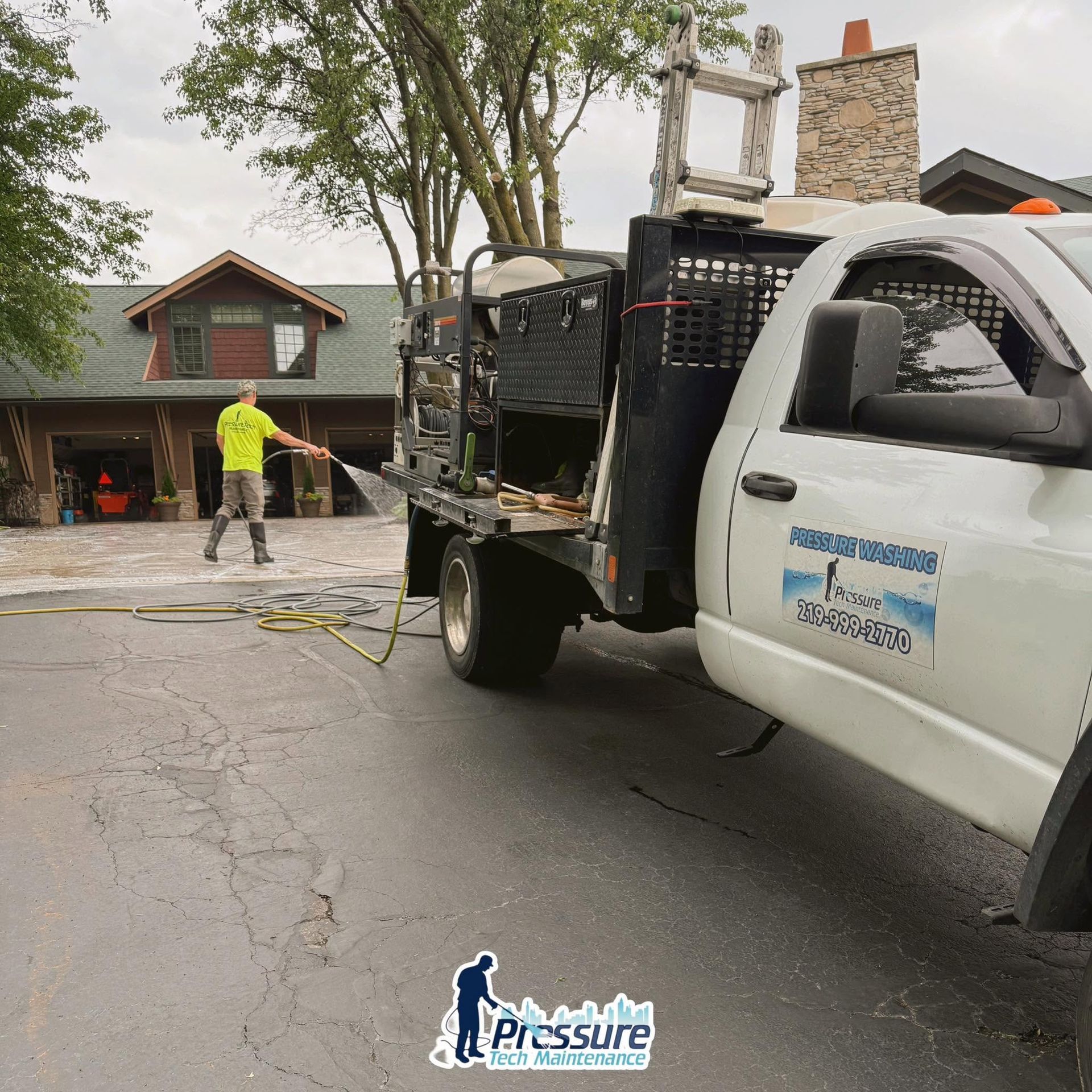 Pressure washing crew cleaning a driveway beside a white truck and house on a rainy street