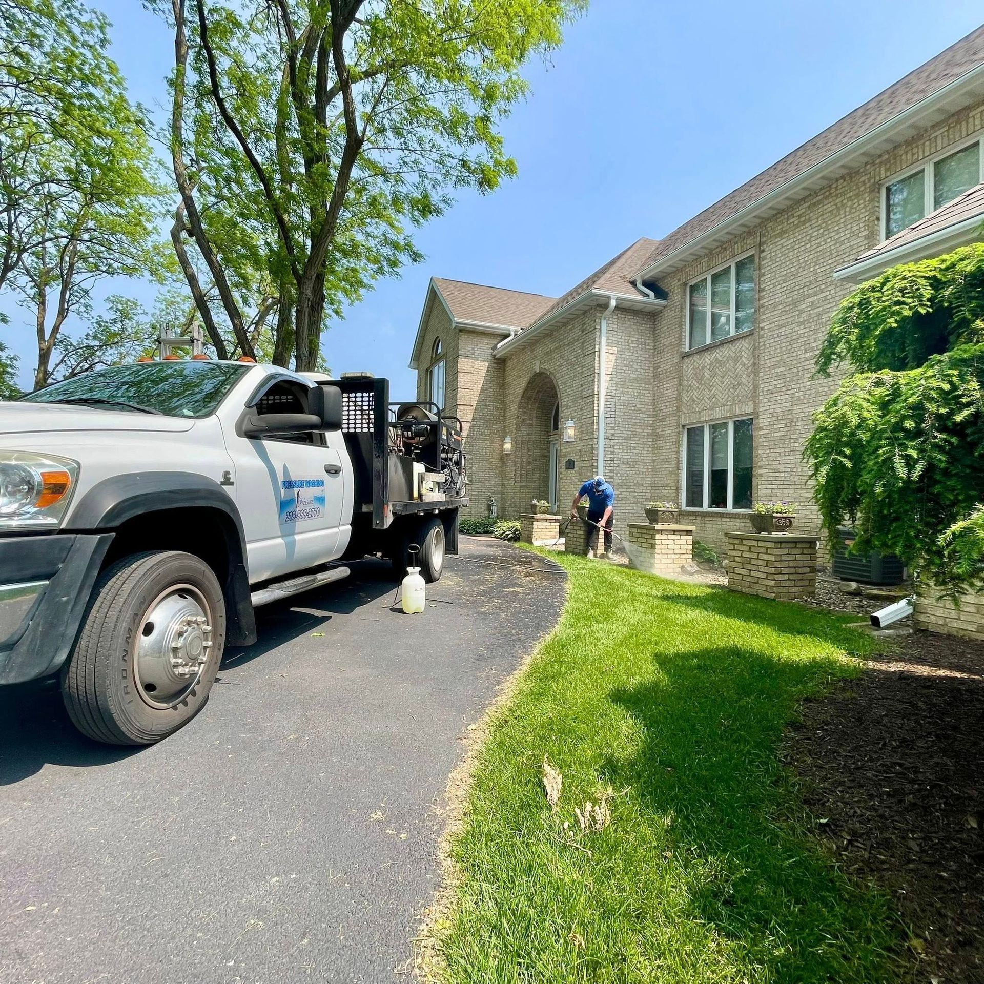 Tow truck parked beside a stone house on a sunny driveway, with a worker near the entrance