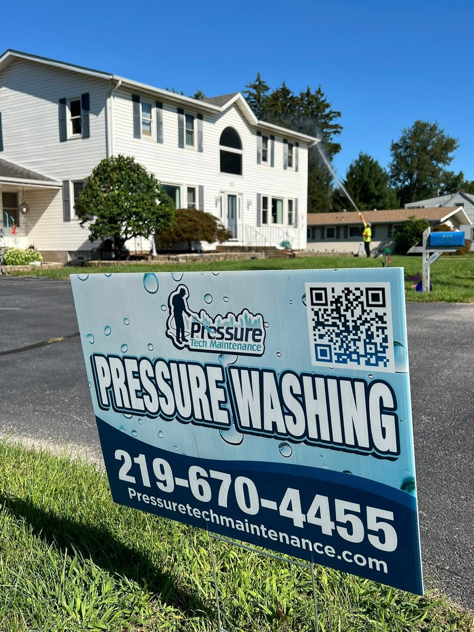 Pressure washing sign in front of a white house on a sunny suburban street, with phone number and QR code.