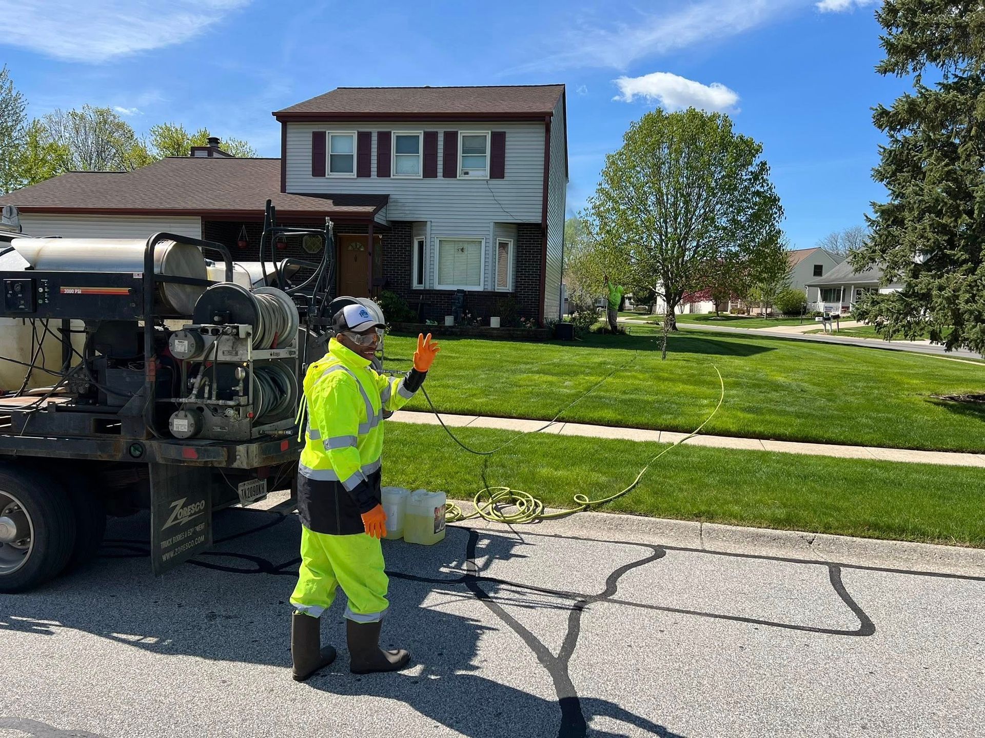 Road worker in neon safety gear standing beside a utility truck on a cracked residential street