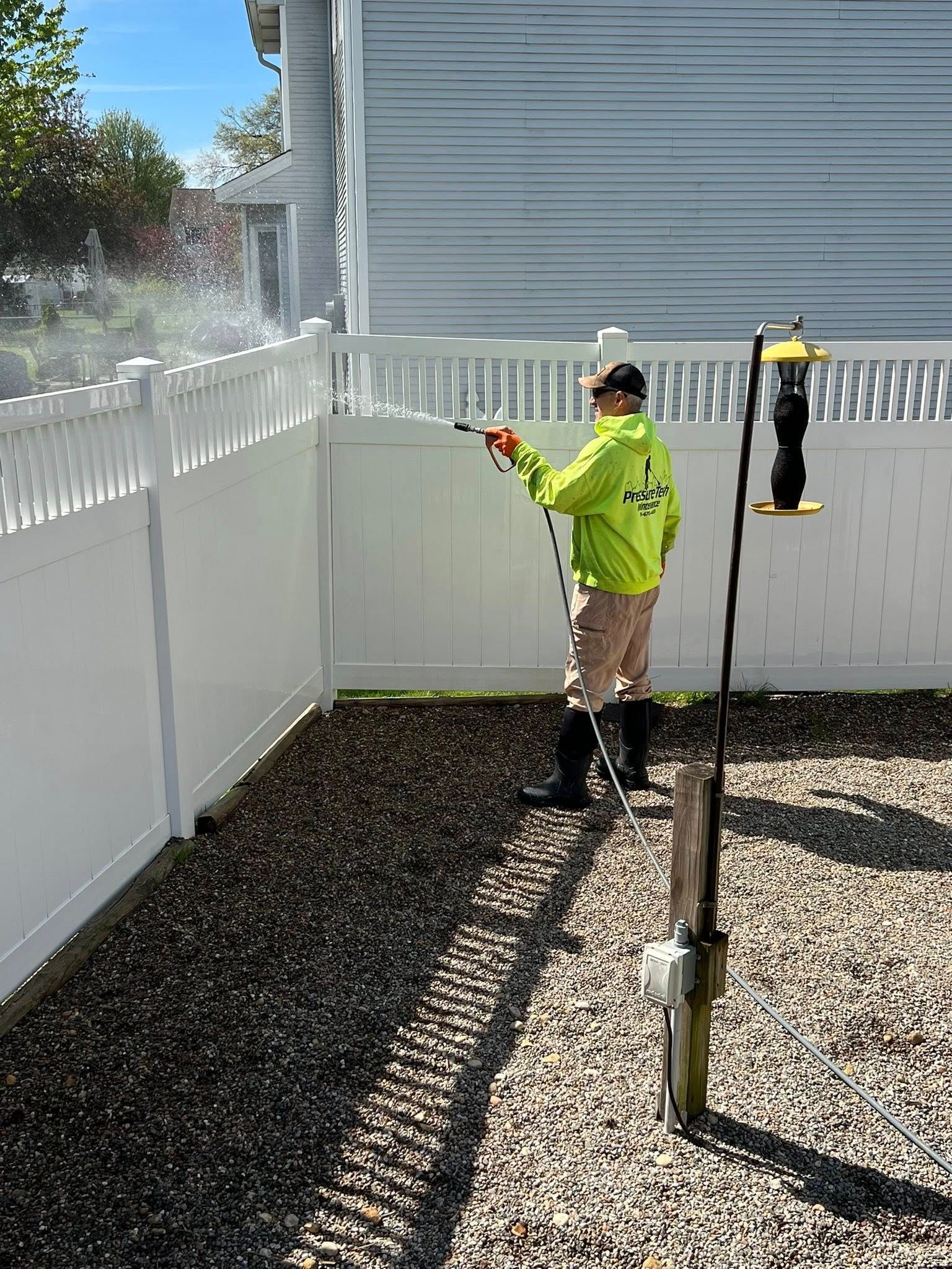 Worker in neon safety jacket installing a white fence beside a gravel yard.