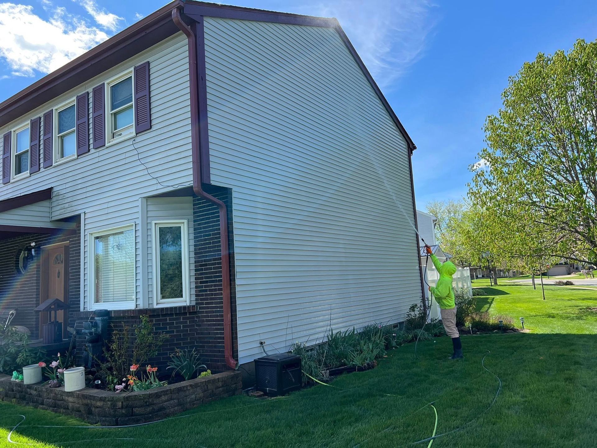 Suburban house with white siding, brick trim, and a person walking beside the lawn