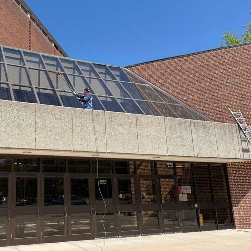Person on a sloped glass roof above a brick building entrance under a blue sky