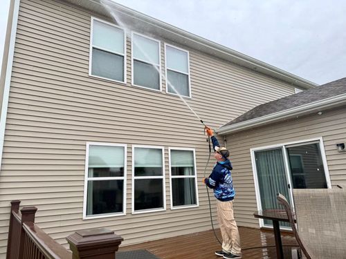 Person on a ladder painting the upper exterior wall of a beige house