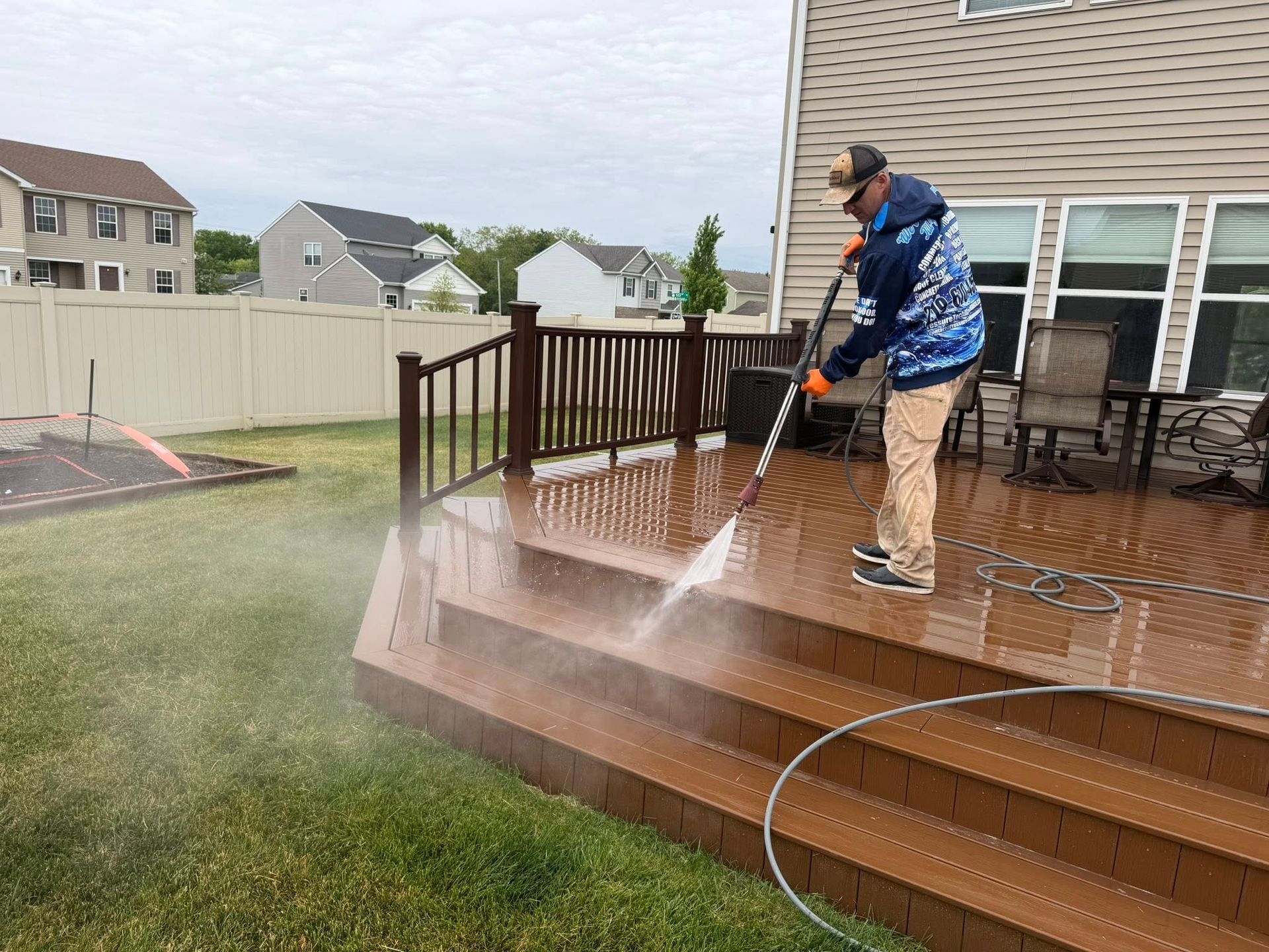 Person pressure-washing a wooden deck beside a house and yard