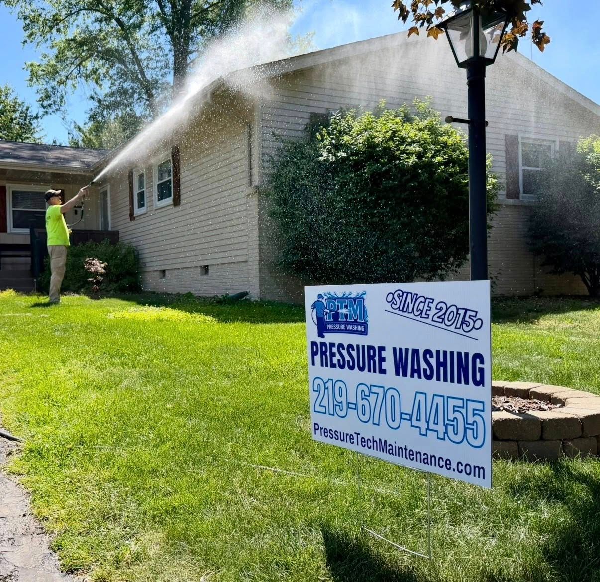 Worker pressure washing a house beside a lawn sign advertising pressure washing services.