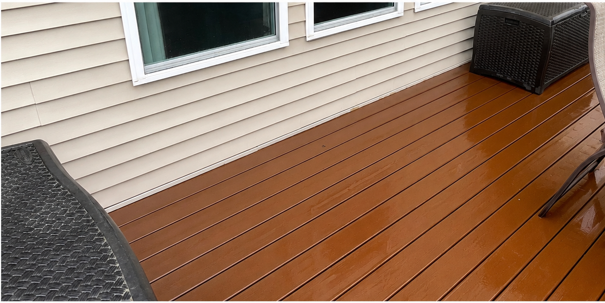 Wooden deck beside a beige house, with two outdoor chairs and windows above the railing.