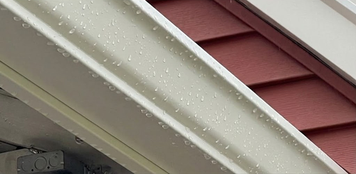 Close-up of white gutter and red roof siding with water droplets