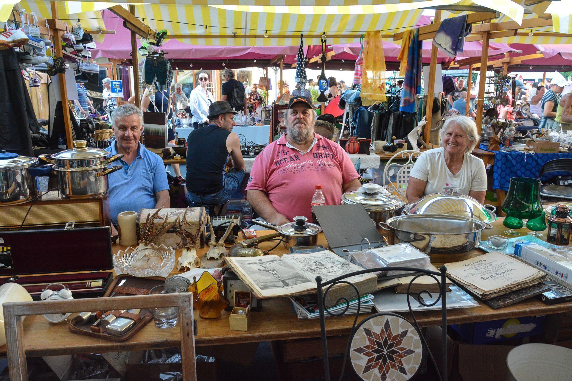 Eine Gruppe von Menschen sitzt auf einem Flohmarkt an einem Tisch.