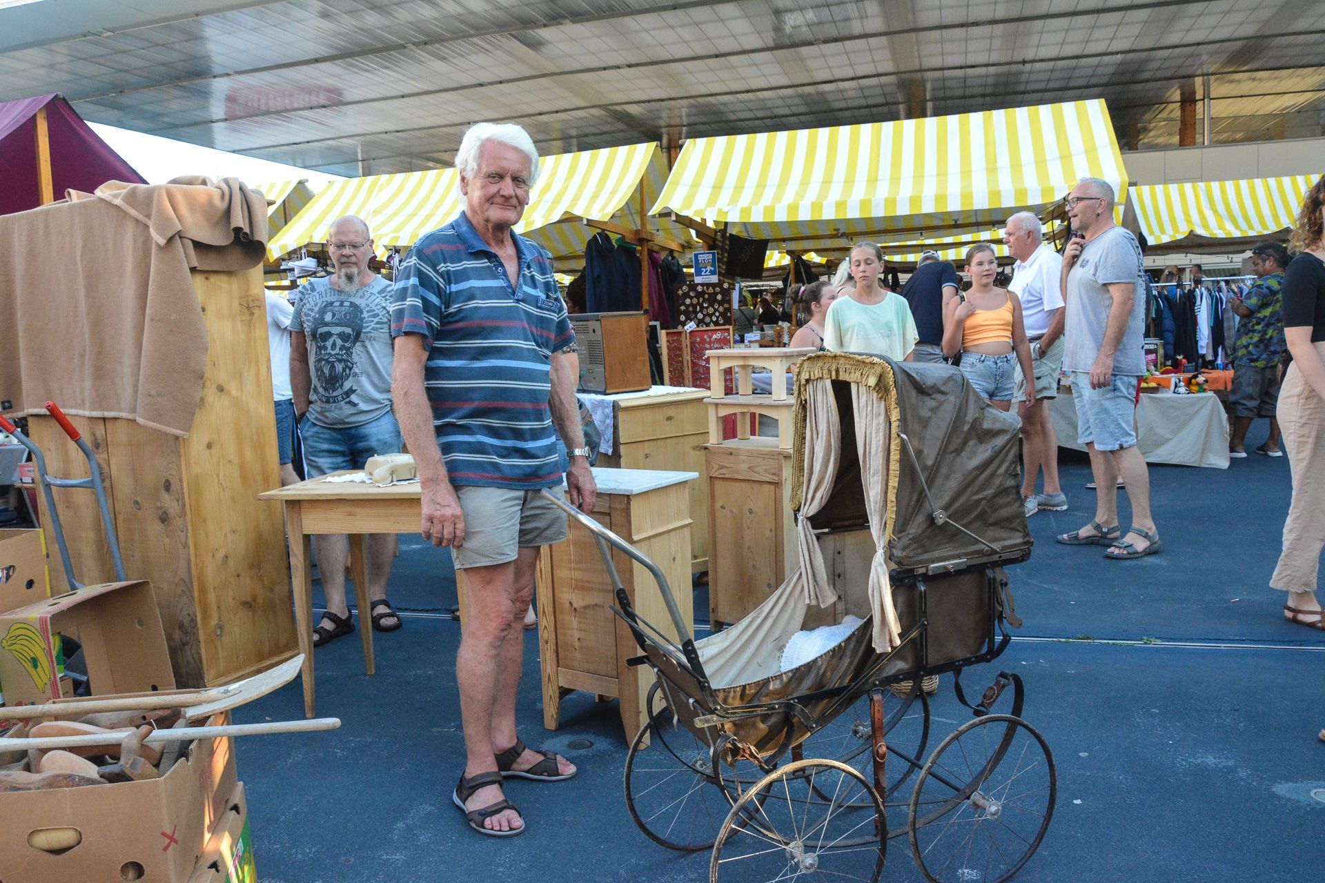 Auf einem Flohmarkt steht ein Mann neben einem alten Kinderwagen.