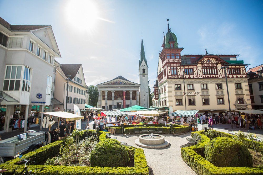 Ein Stadtplatz mit einem Brunnen in der Mitte und einer Kirche im Hintergrund.