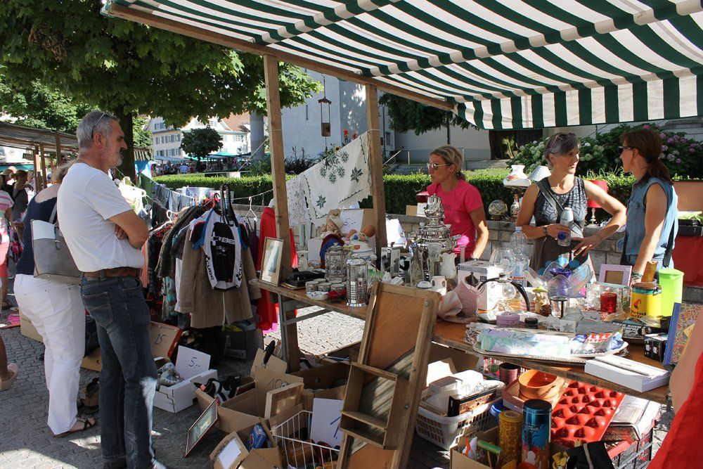 Eine Gruppe von Menschen steht unter einem gestreiften Zelt auf einem Flohmarkt.
