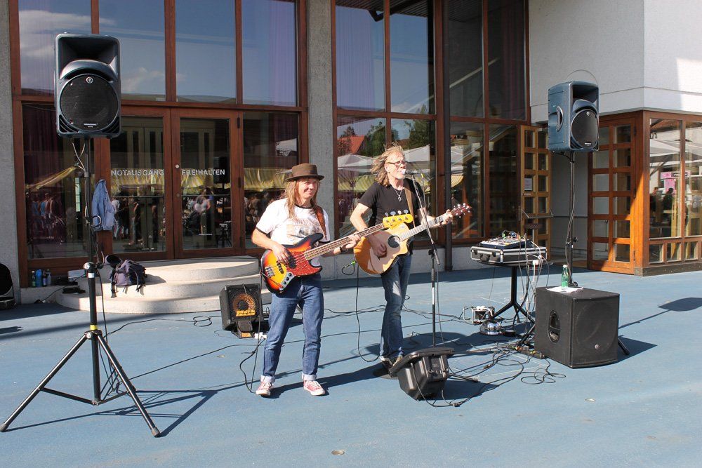 Zwei Personen, die auf einer Bühne Gitarre spielen und in Mikrofone singen