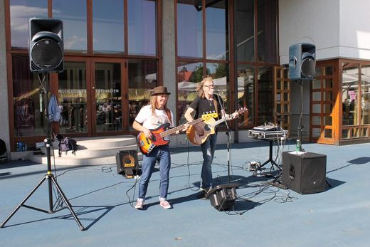 Zwei Personen, die auf einer Bühne Gitarre spielen und in Mikrofone singen