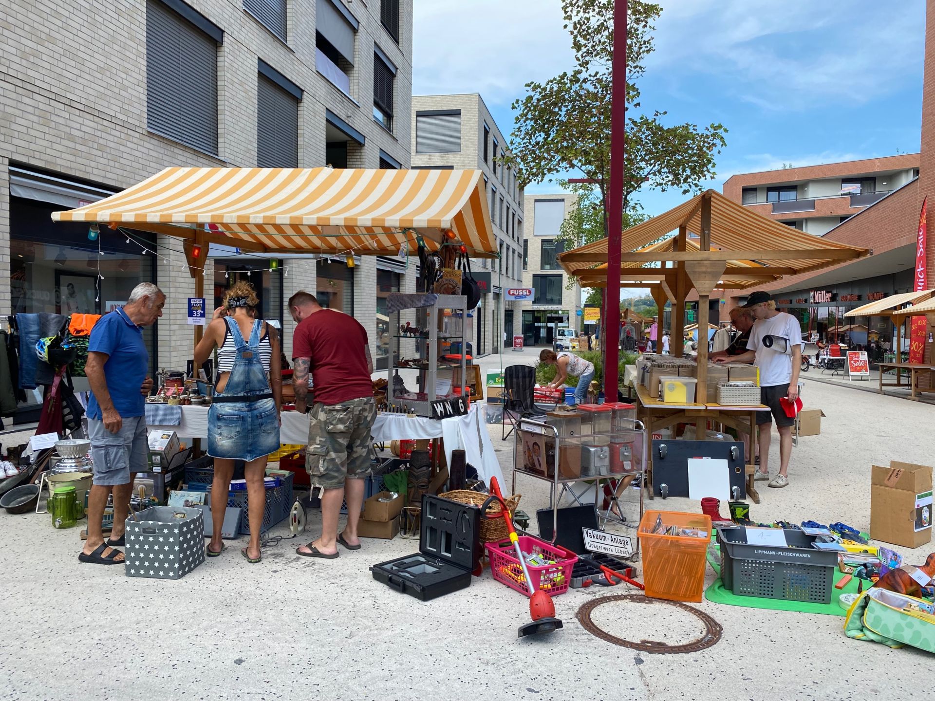 Eine Gruppe von Menschen steht unter einem Zelt auf einem Flohmarkt.