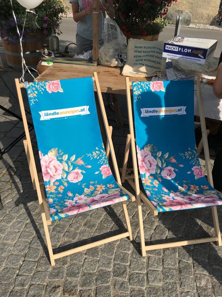Zwei Gartenstühle mit Blumen darauf stehen auf einer Kopfsteinpflasterstraße.