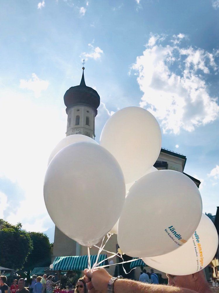 Eine Person hält einen Haufen weißer Luftballons vor einer Kirche.