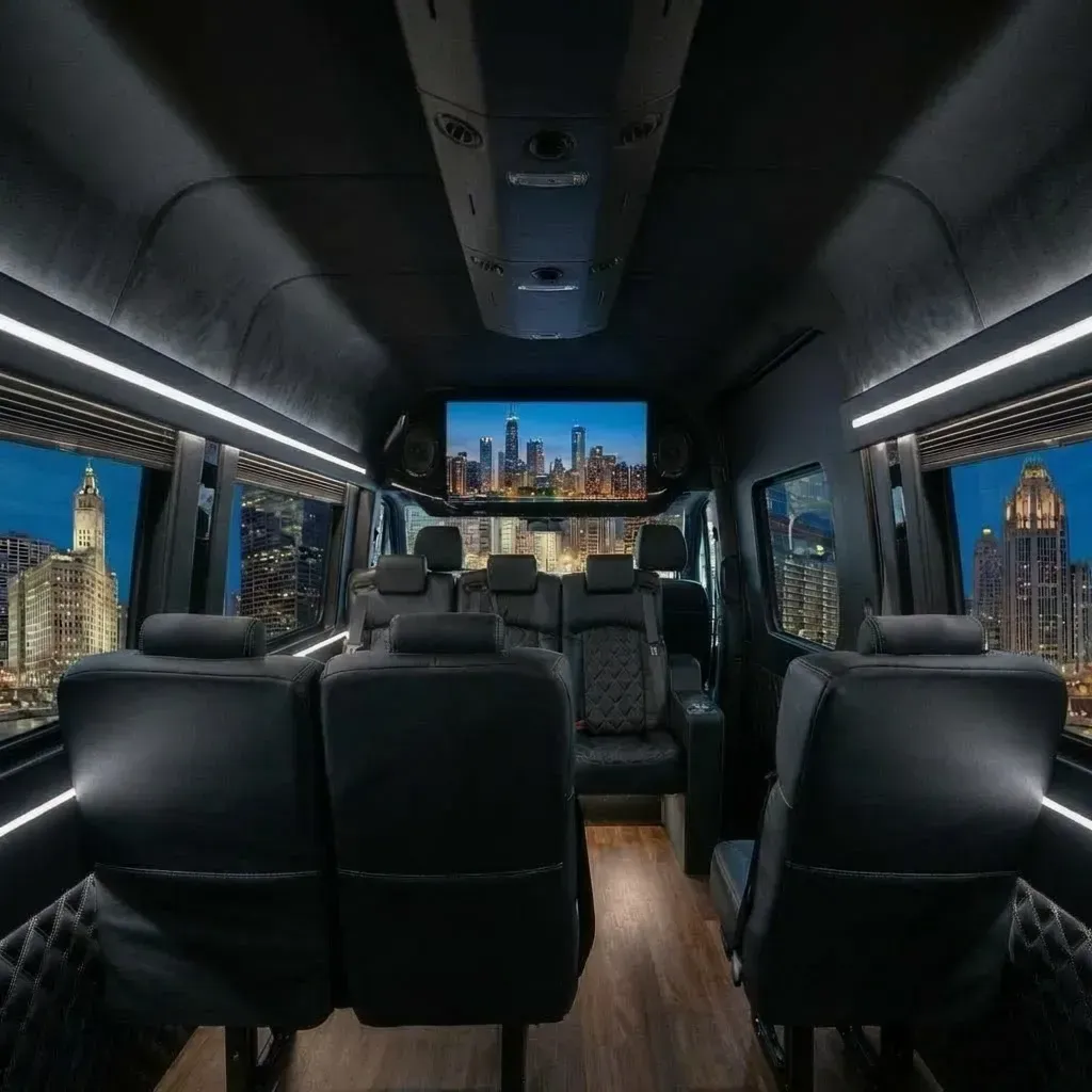 Interior of a black luxury van with leather seating, a TV, and city views through the windows.
