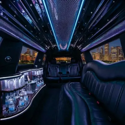 Interior of a black limousine with leather seats, a lit bar, and city skyline visible through the windows.