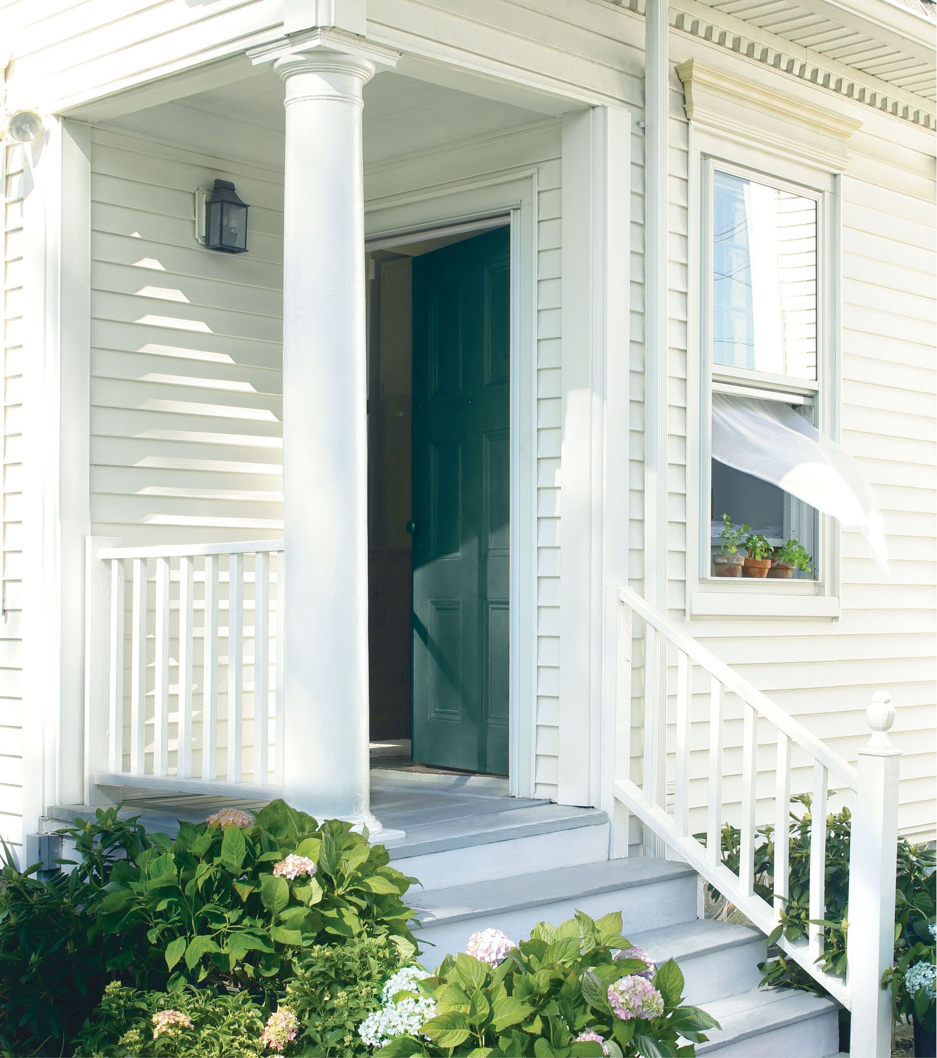 A front porch with white clapboard siding, a green door, a white column, stairs, and hydrangeas in front.