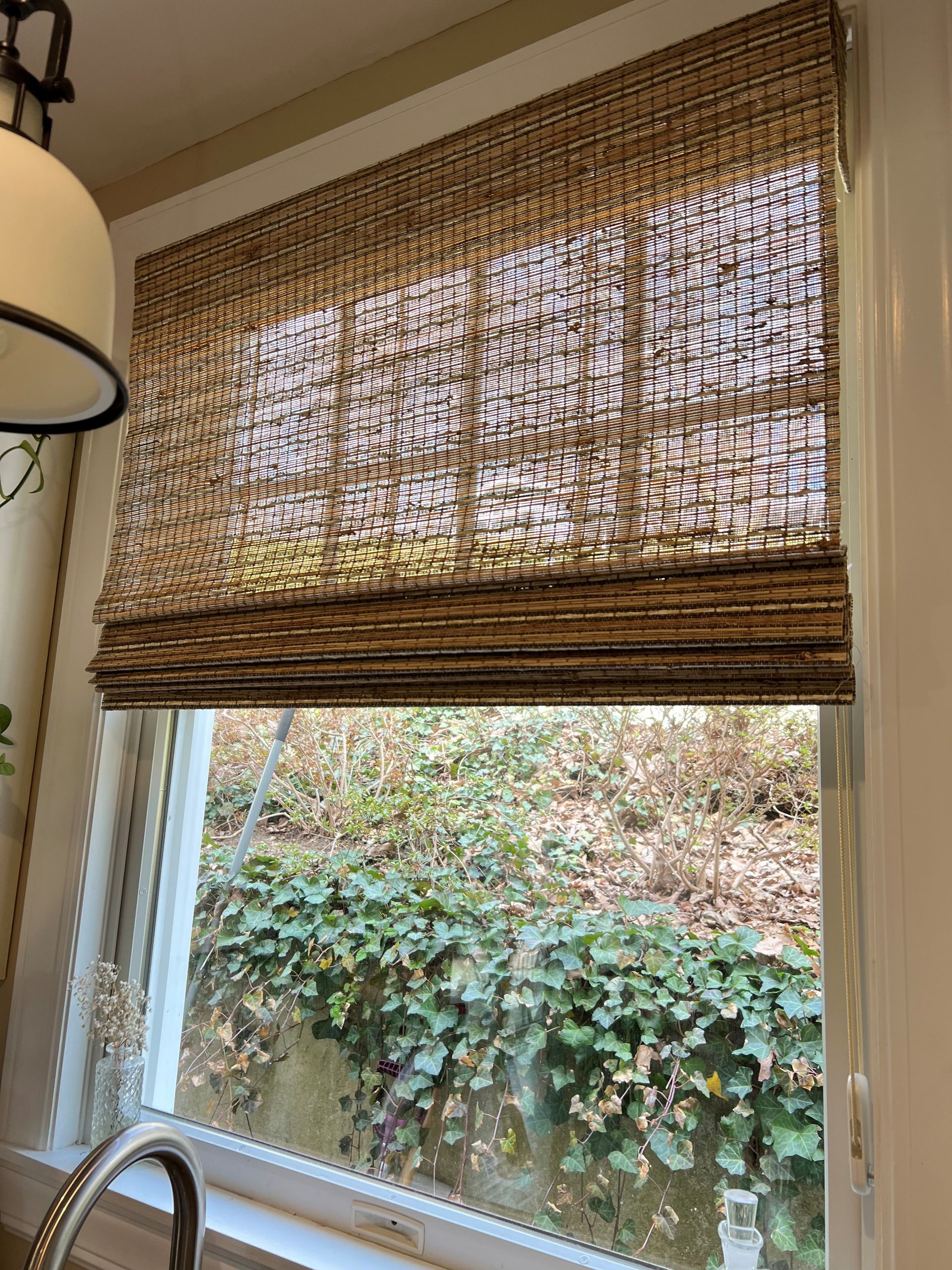 Kitchen window with woven bamboo blinds and a view of greenery outside.