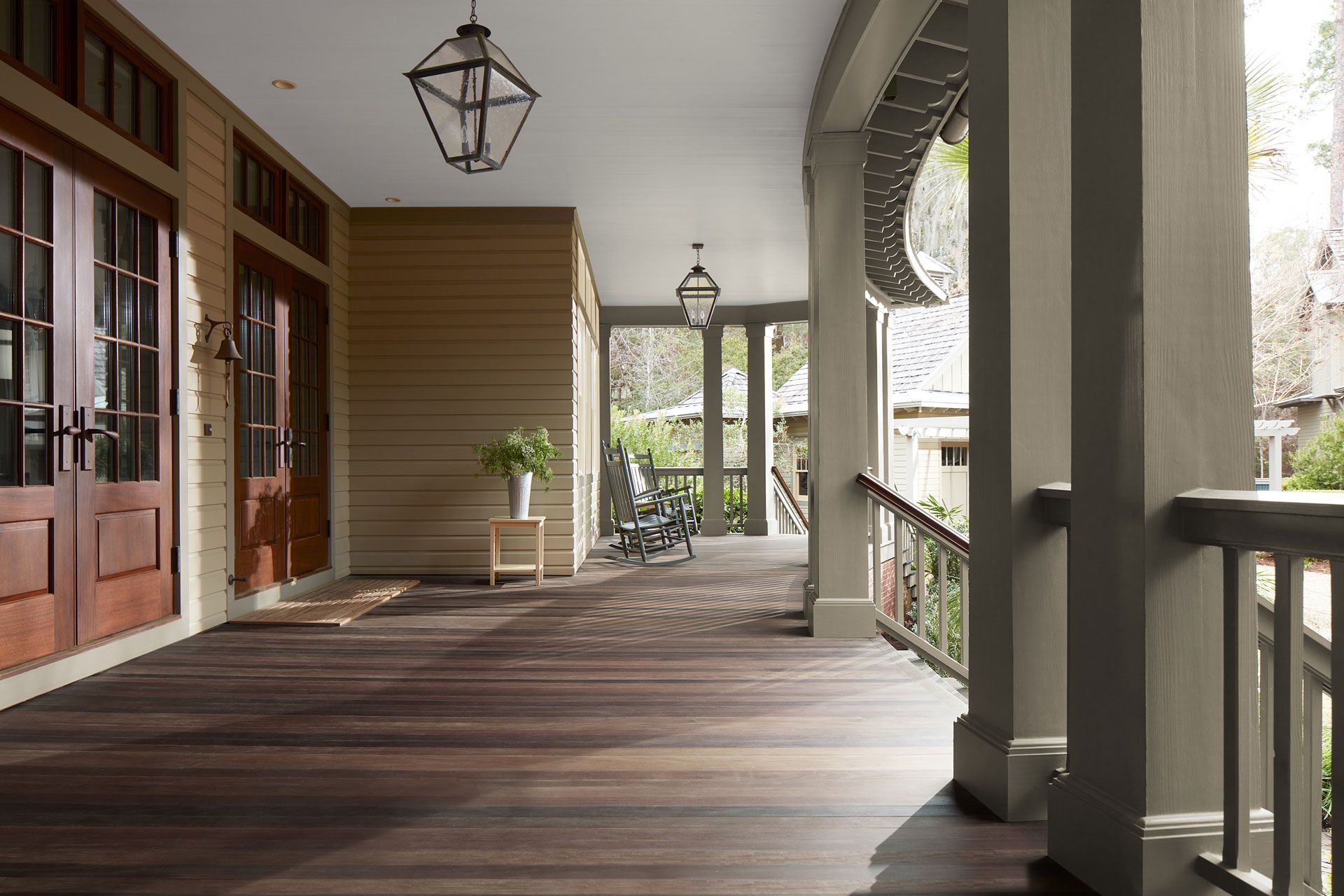 A spacious wooden deck with columns and a railing overlooking a bright, landscaped outdoor area.