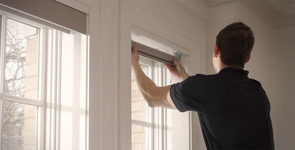Person installing a window blind in a bright white room