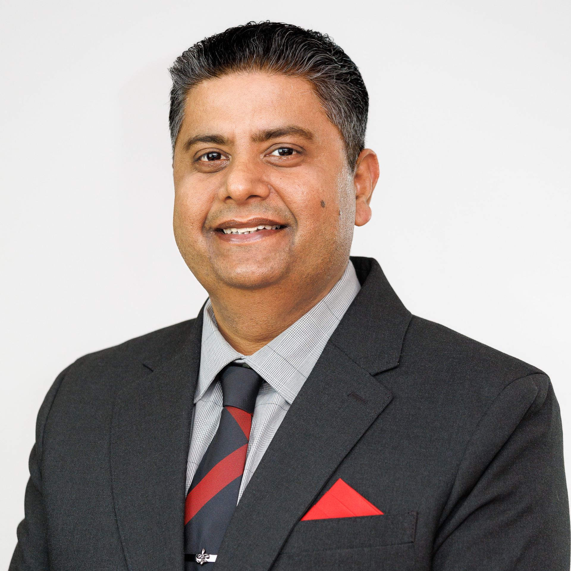 Man in a suit smiles, red pocket square, striped tie, against a white background.