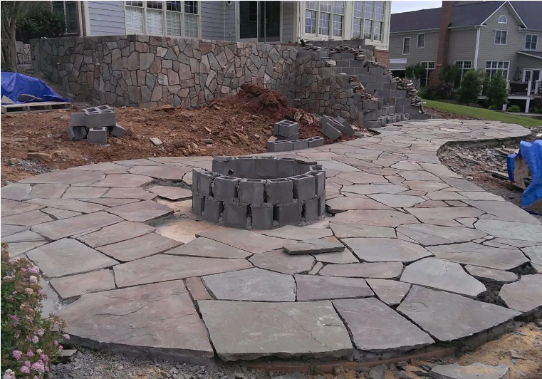 Stone patio with a circular fire pit in a residential backyard under construction