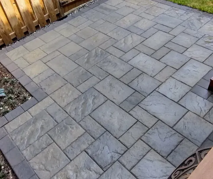 Gray stone paver patio laid in a herringbone pattern beside a wooden fence