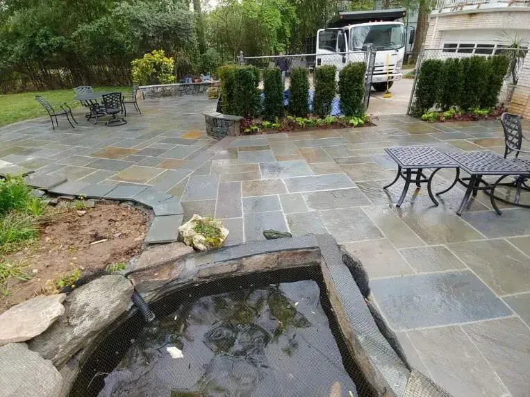 Stone patio with a small pond, black benches, potted shrubs, and a parked vehicle in the background