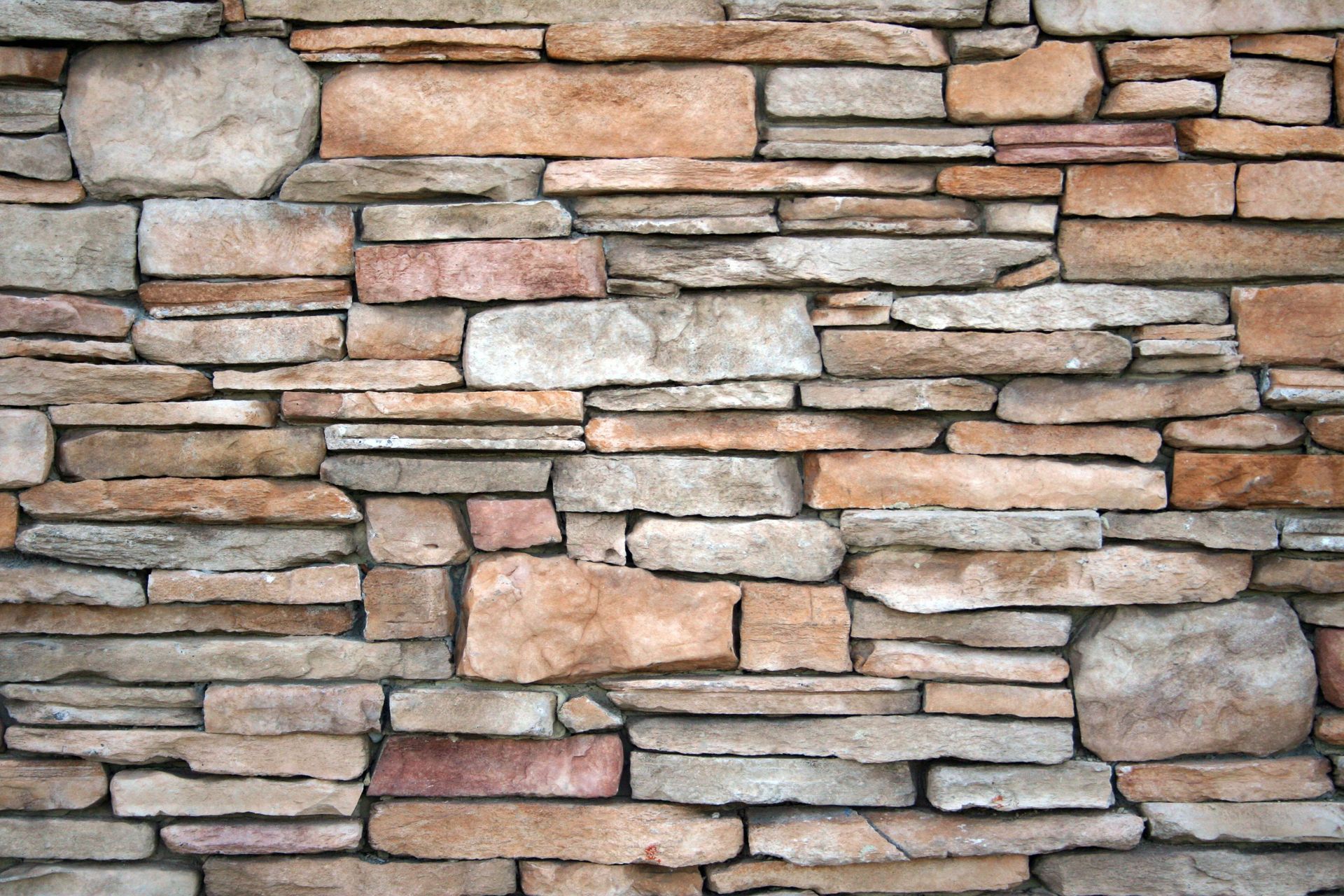 Stacked tan, gray, and pink stones forming a rustic stone wall texture.