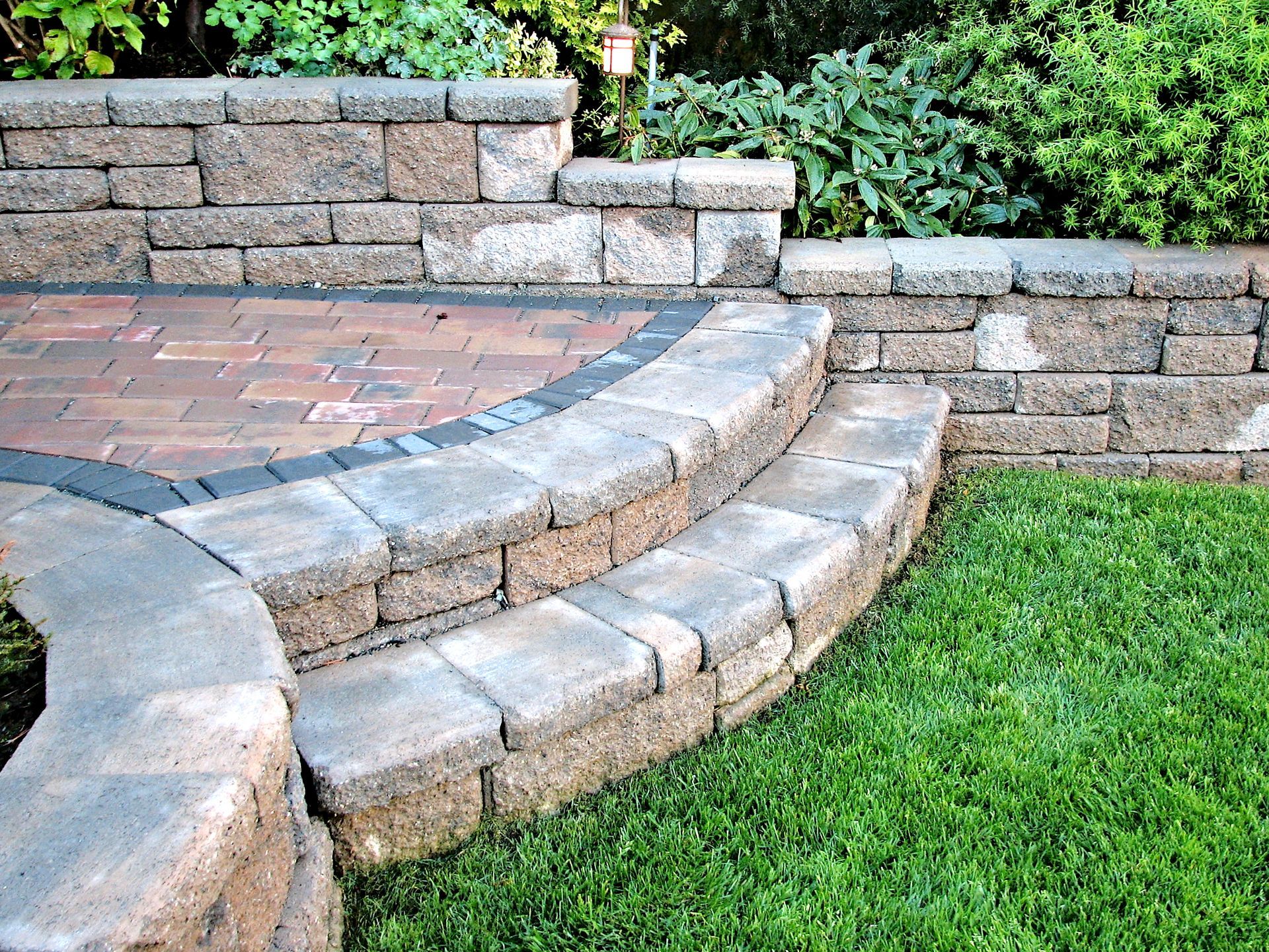 Curved stone steps leading to a brick patio beside a green lawn and retaining wall