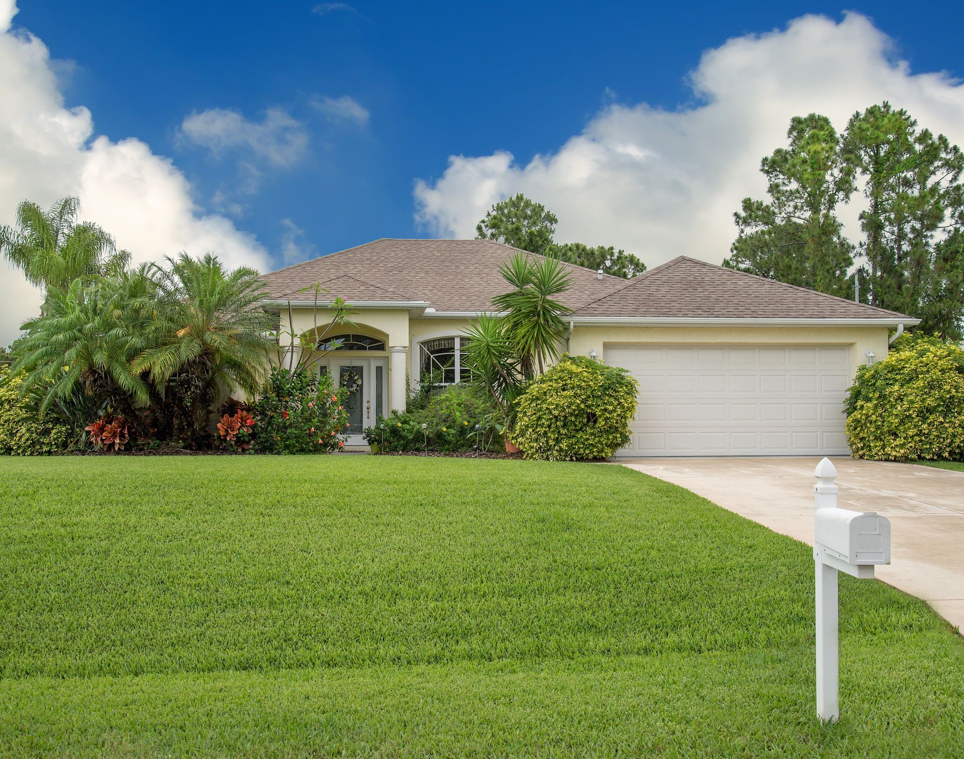 Suburban house with white garage, tiled roof, lush green lawn, and a mailbox under a blue sky
