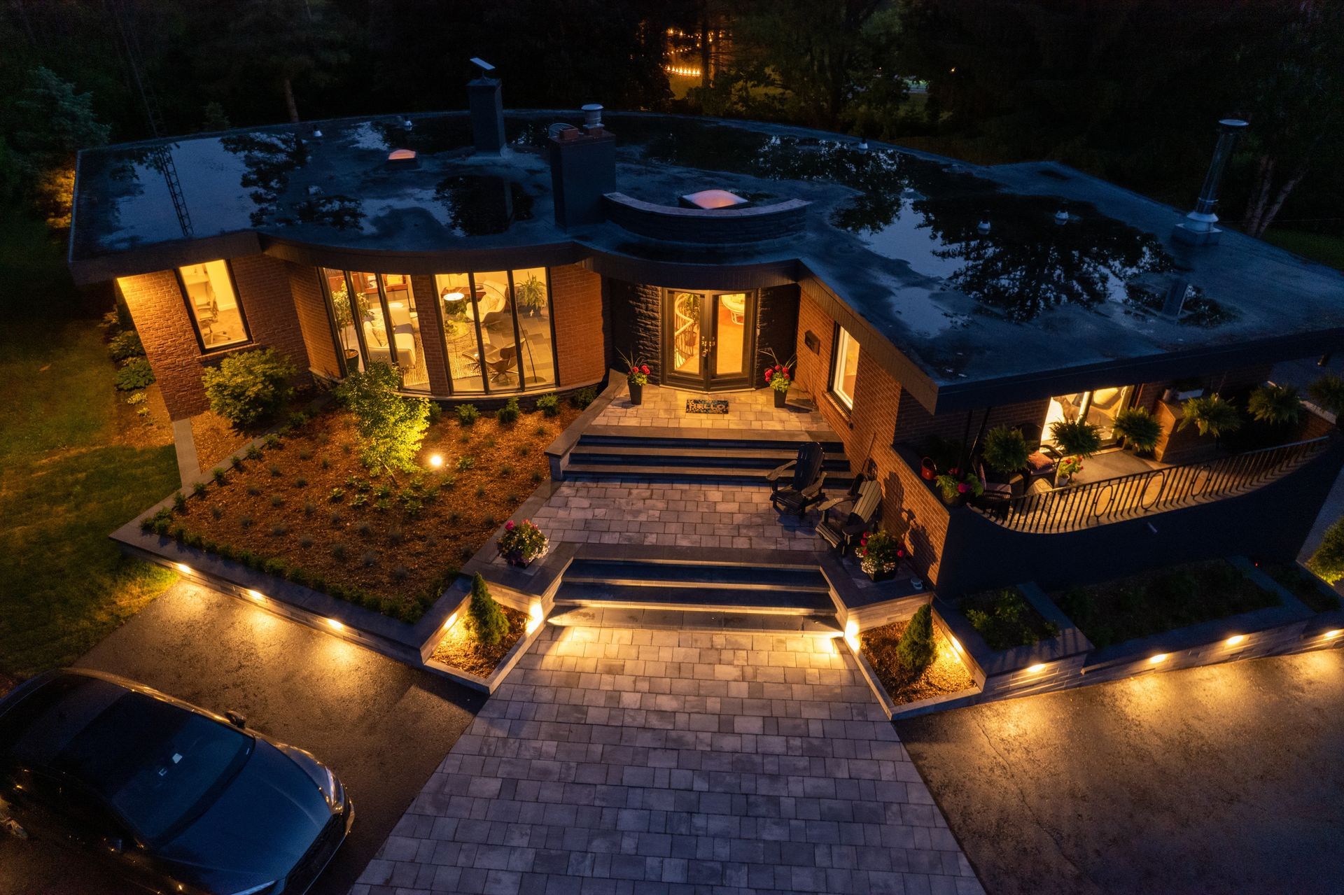 Warmly lit modern house at night with stone walkway, steps, and landscaped garden lights