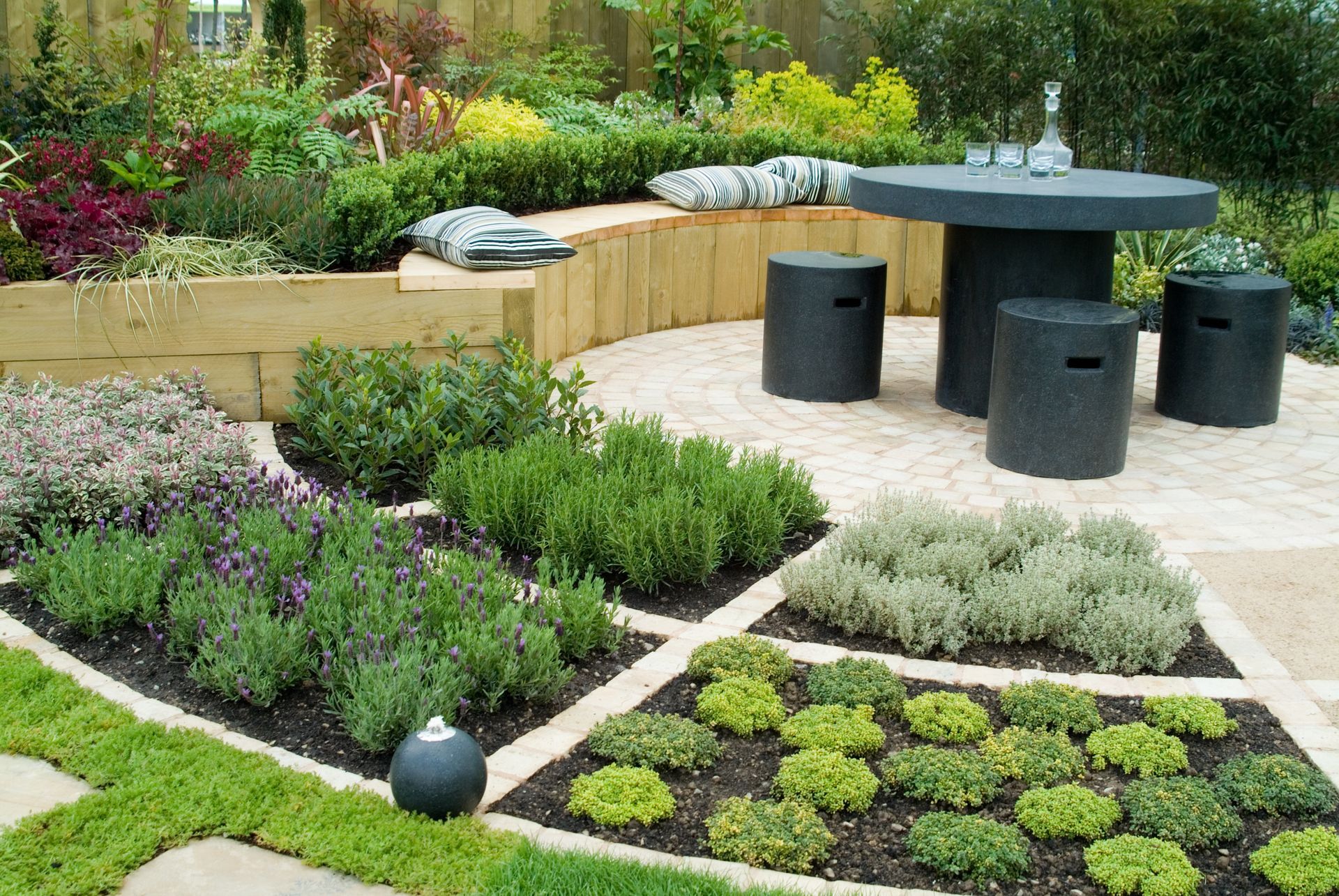Modern garden patio with black table and stools, raised flower beds, and patterned greenery