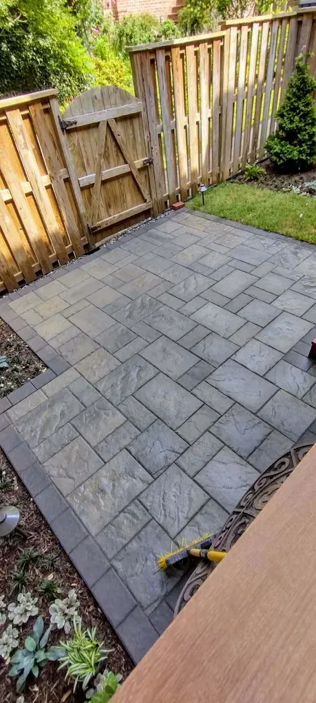 Backyard patio with gray paver stones and a wooden fence, with a small grass border.