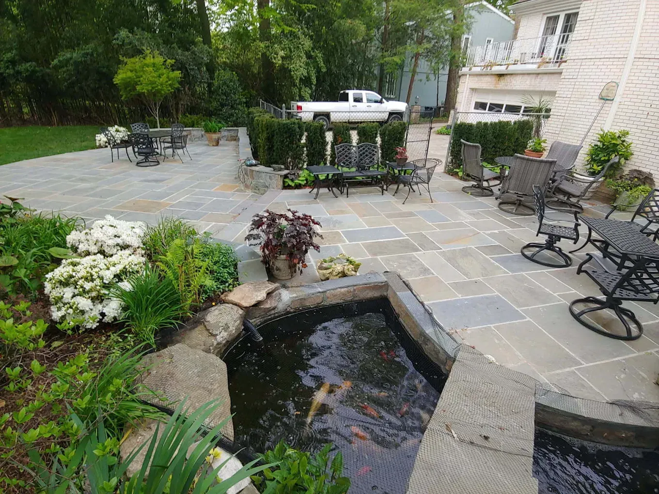 Backyard patio with a pond, stone walkway, chairs, and flowering plants