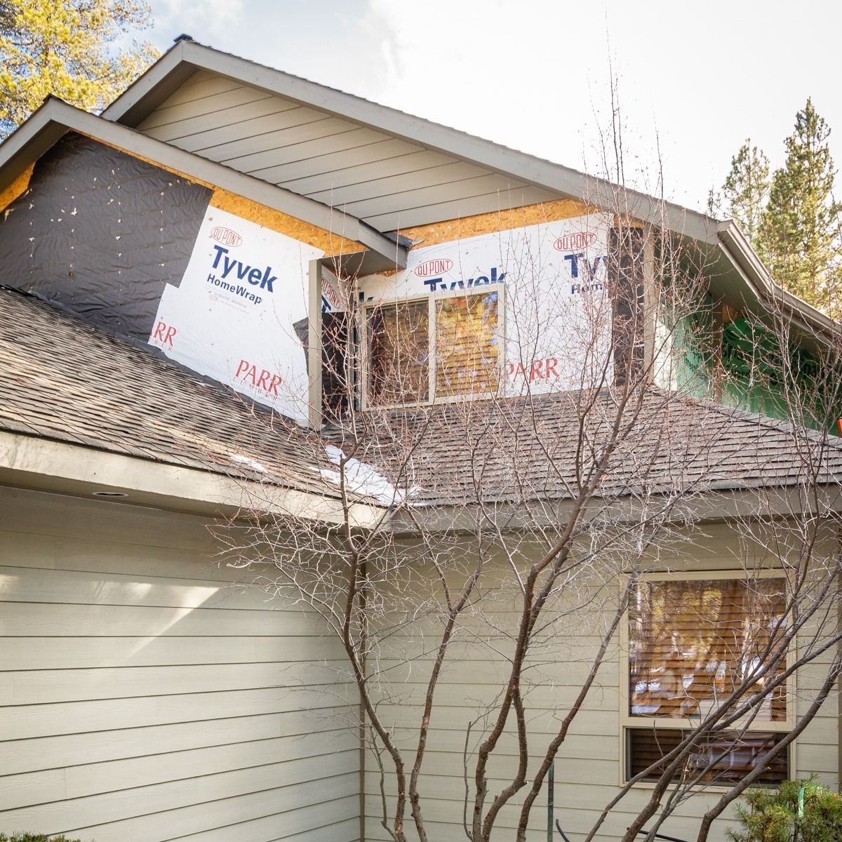 House under construction with exposed Tyvek wrap and roof shingles.