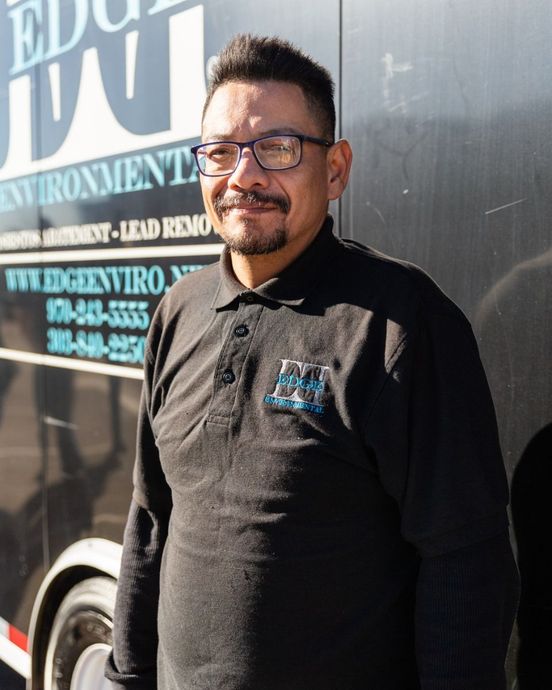 Man in black shirt with glasses, standing in front of a truck with business logo; posing.