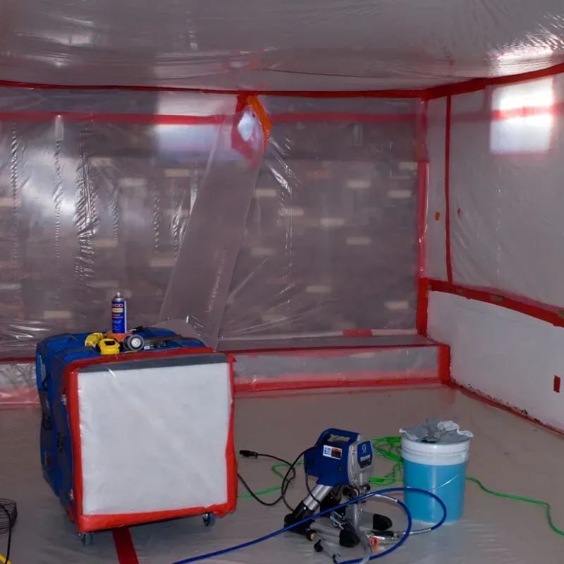 Inside containment, air scrubber and equipment are set up for remediation work. Walls and floor sealed with plastic.