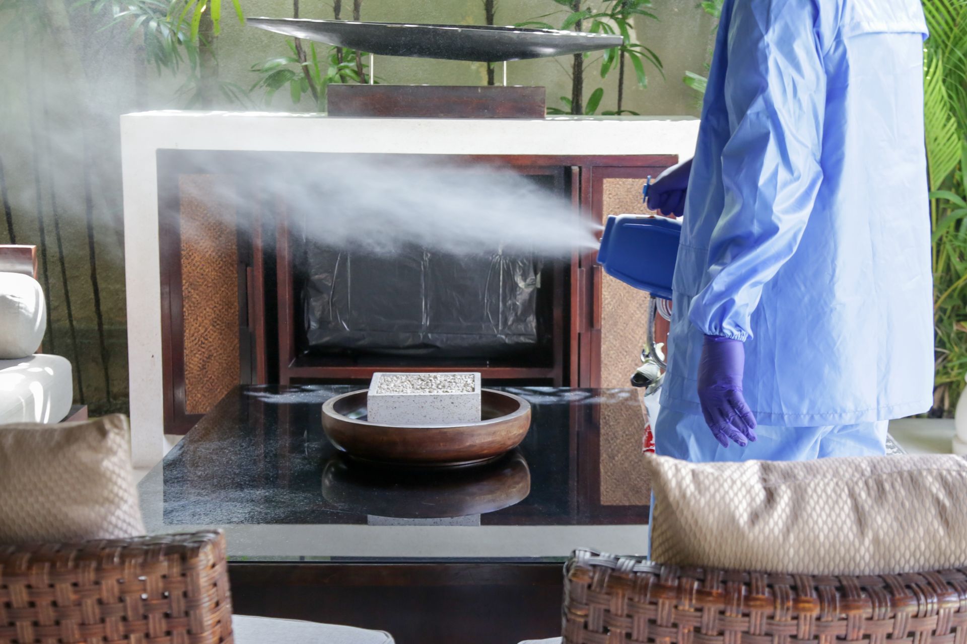 Person in blue protective suit spraying disinfectant on a counter with decor.