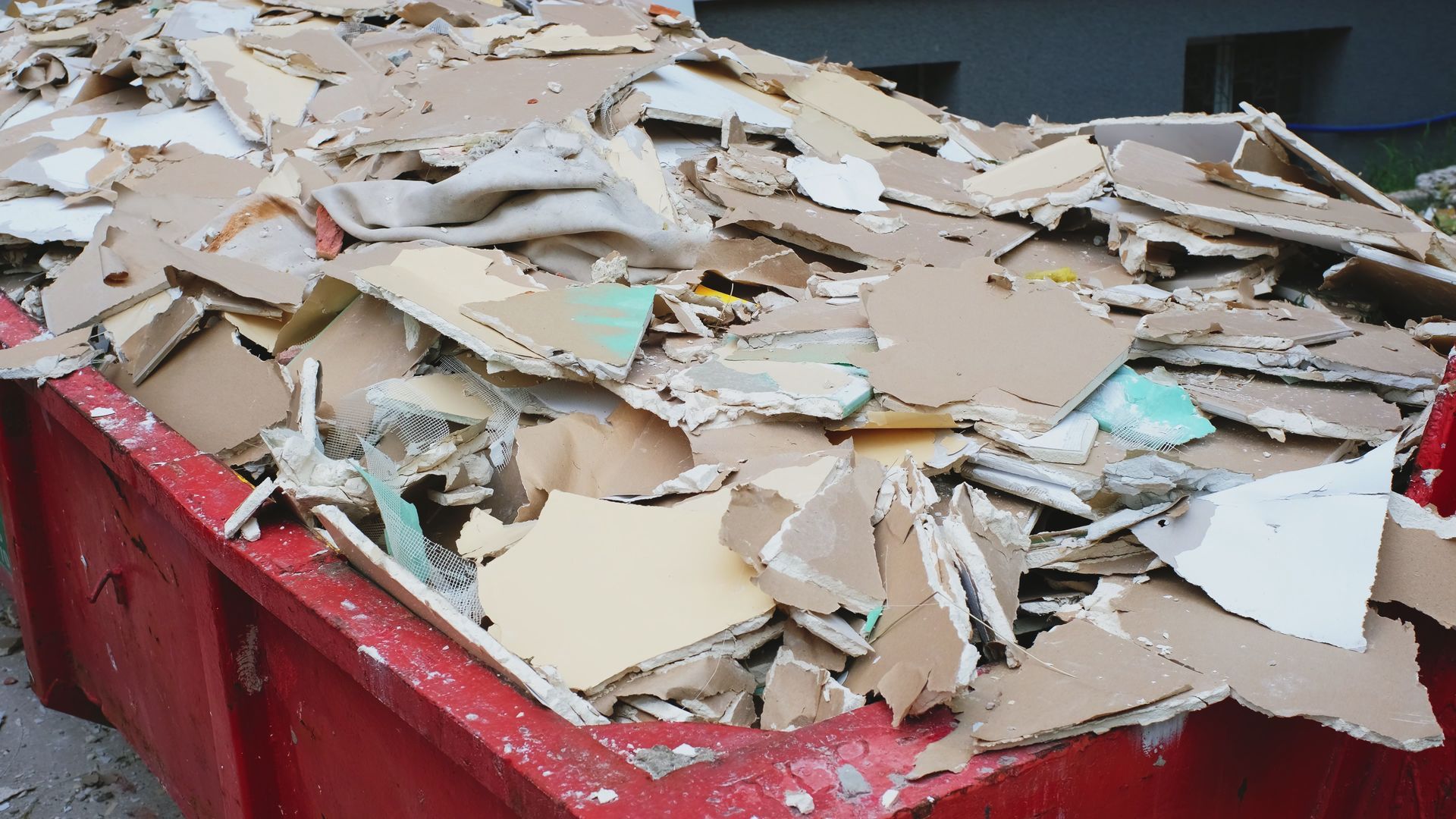 Red dumpster filled with torn drywall pieces from a construction site.