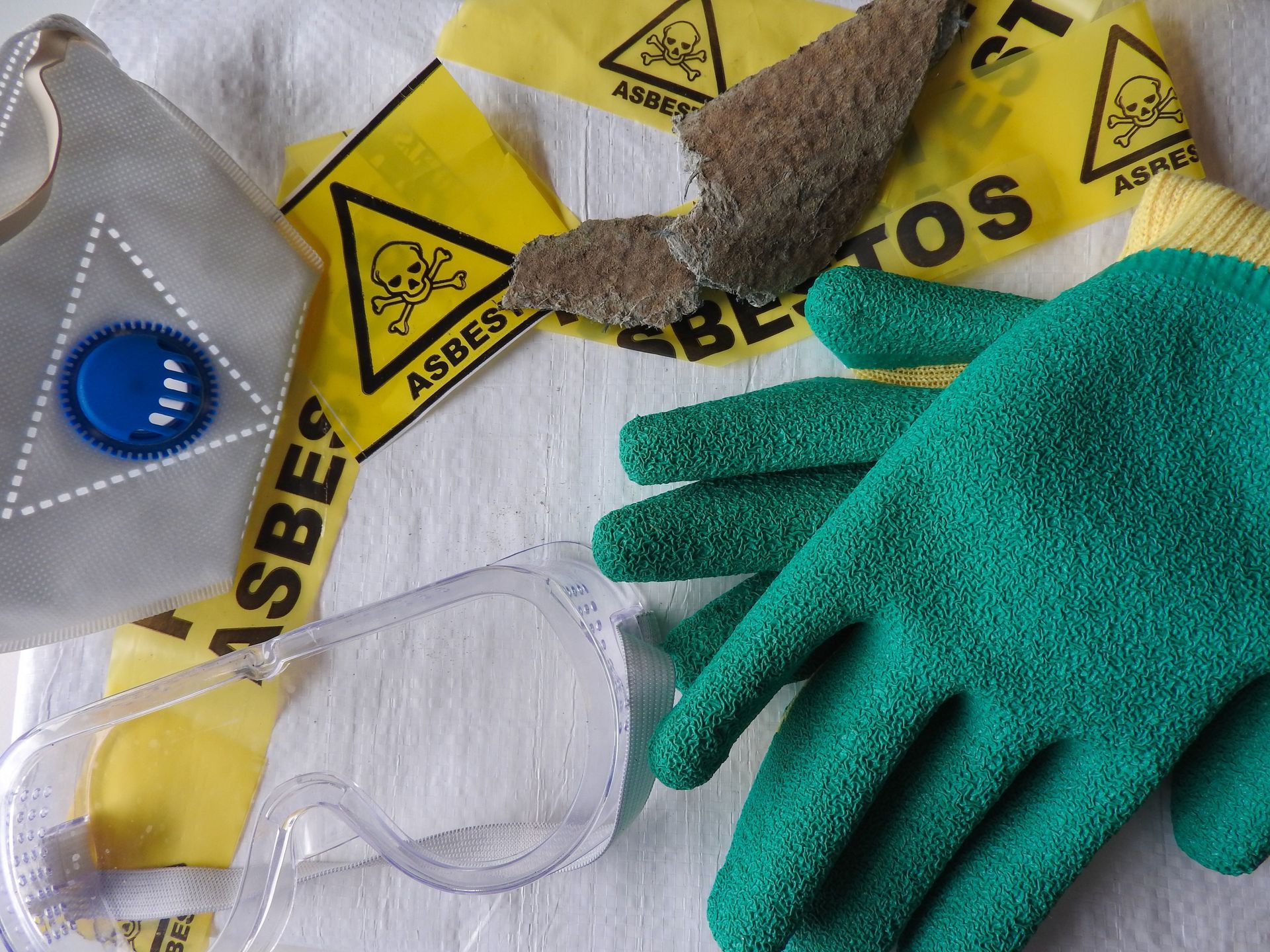 Asbestos safety equipment: respirator, goggles, gloves, warning tape, and sample.