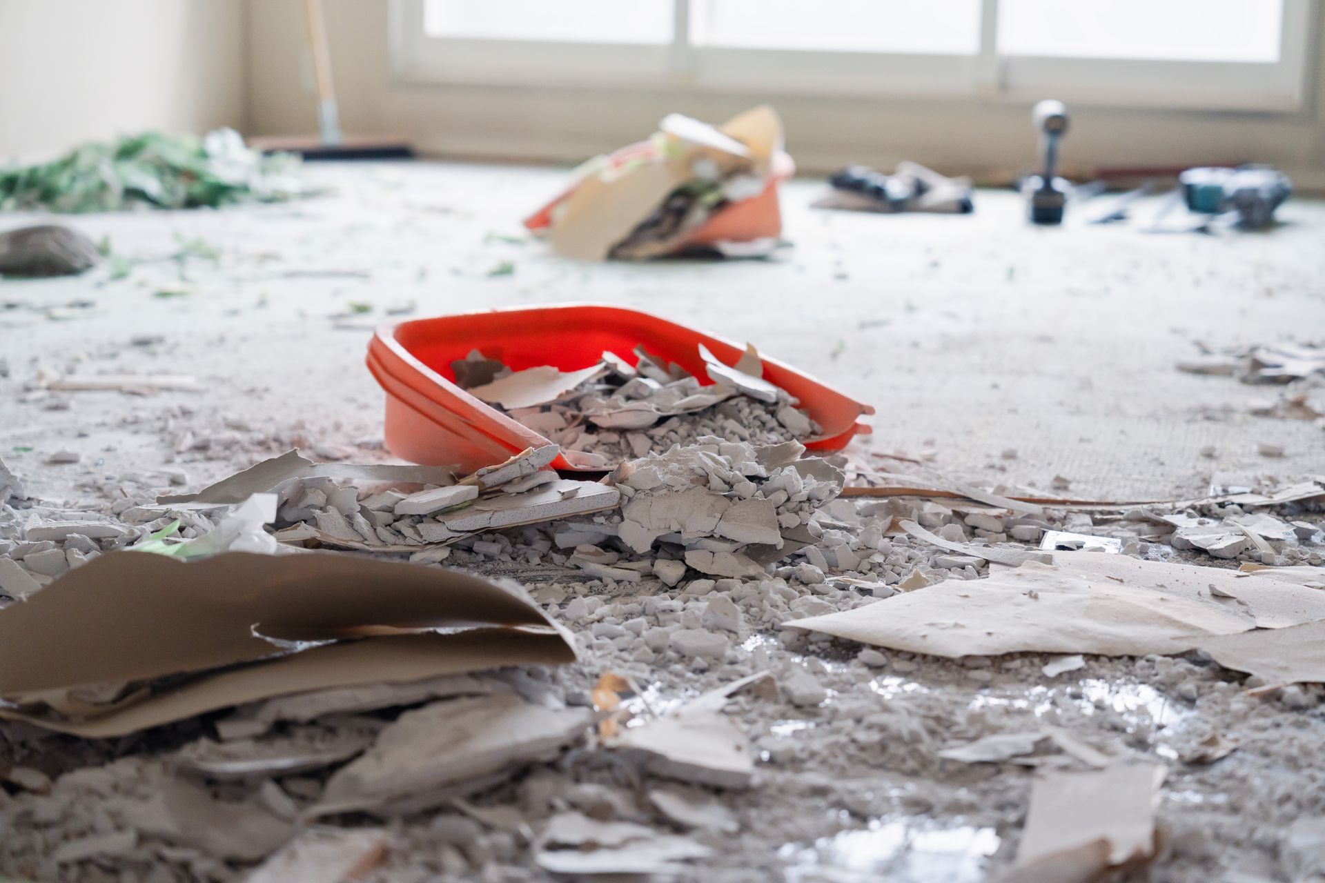Construction debris on a floor with a red dustpan near a window.